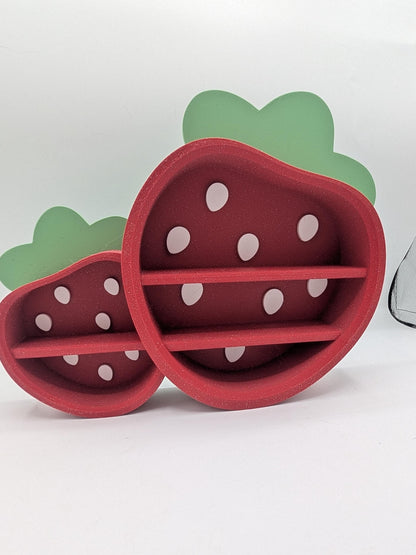 Strawberry Trinket Shelf angled view — 3D printed red strawberry display shelves with white seed details and green leaf tops, large and small sizes