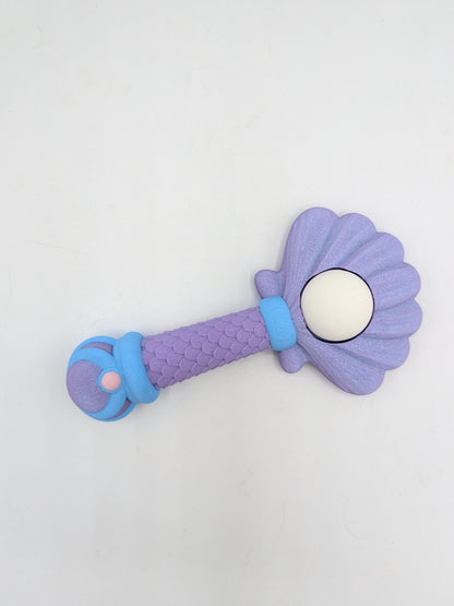 Mermaid wand clicker fidget lying flat showing shell-shaped top, pearl detail, and blue accent bands