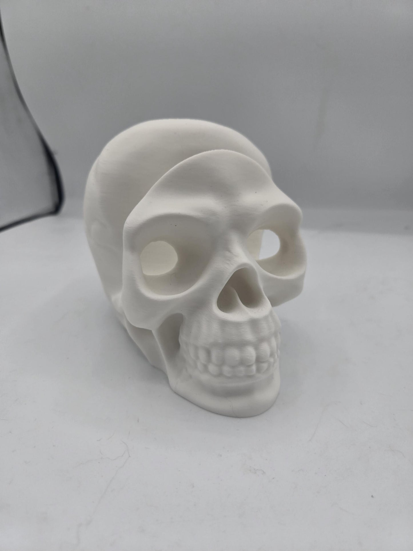 White 3D printed human skull glasses holder shown without glasses, front three-quarter view