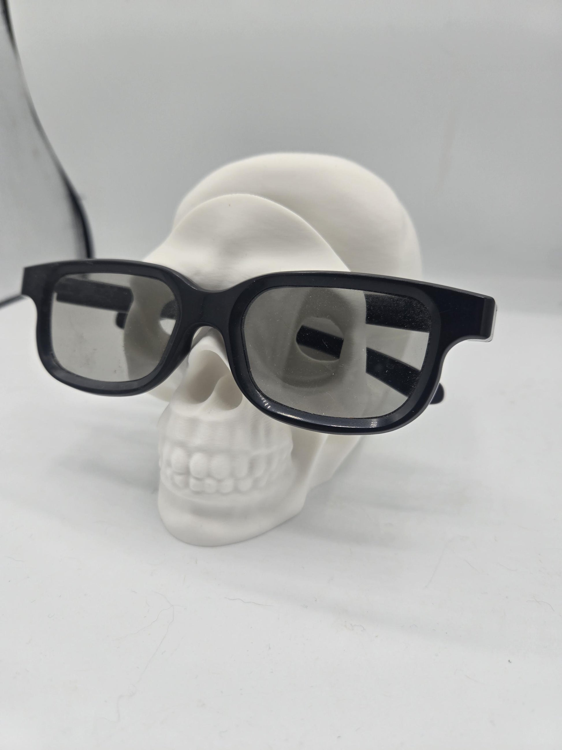 White human skull glasses holder displaying black eyeglasses on its face, spooky desk decor