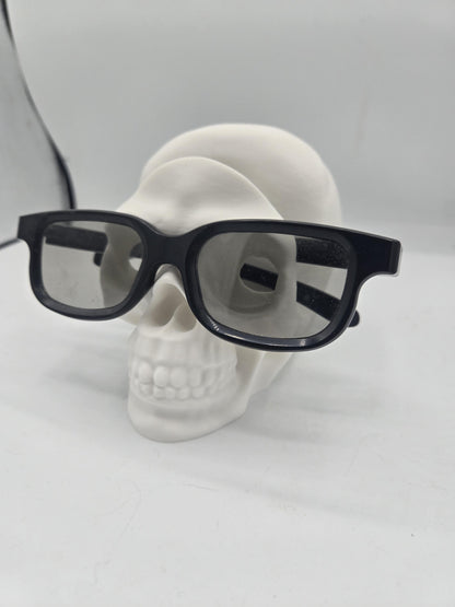 White human skull glasses holder displaying black eyeglasses on its face, spooky desk decor