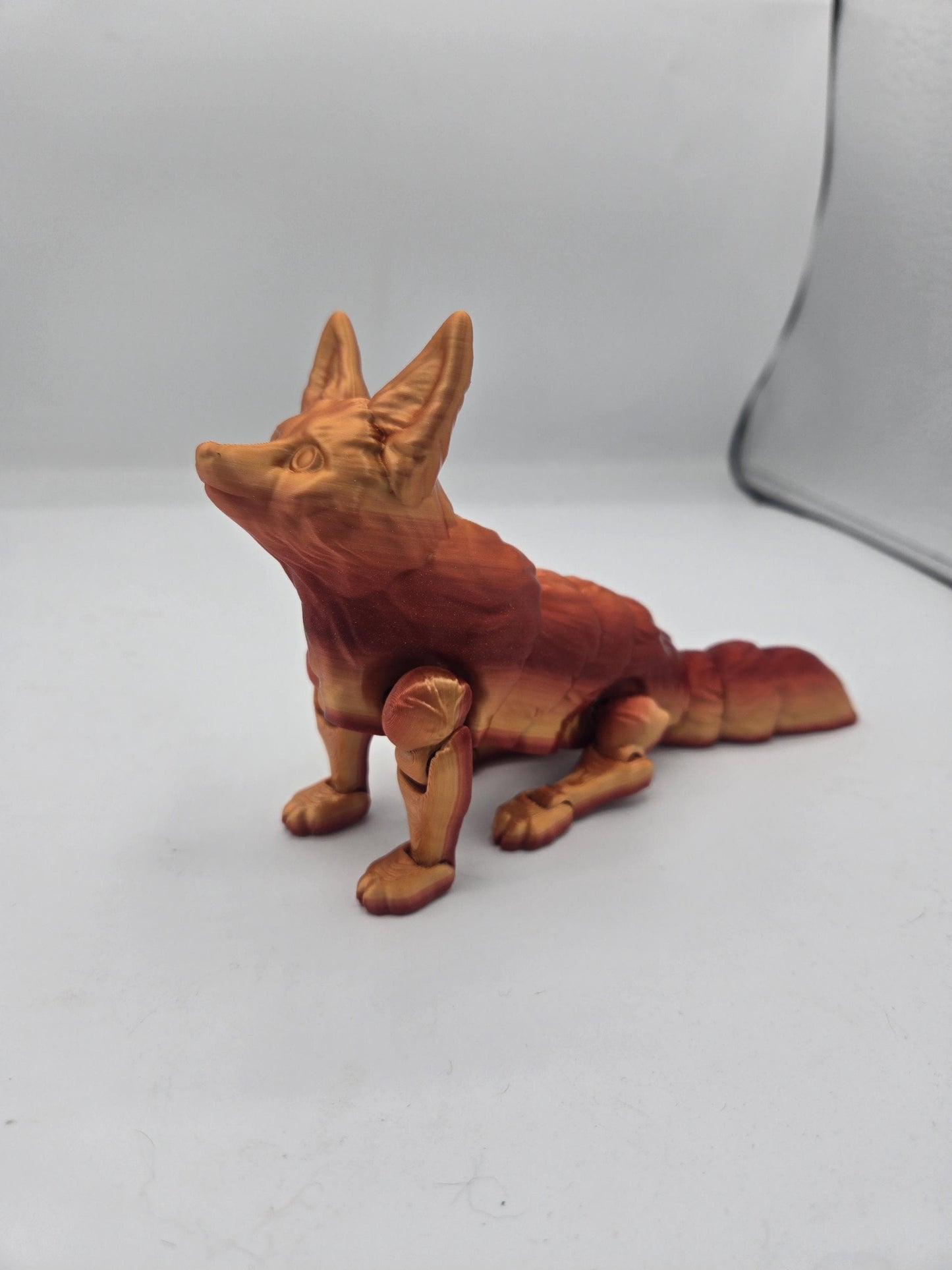 Red and gold fennec fox flexi figurine seated with head raised, showing jointed legs and fur texture