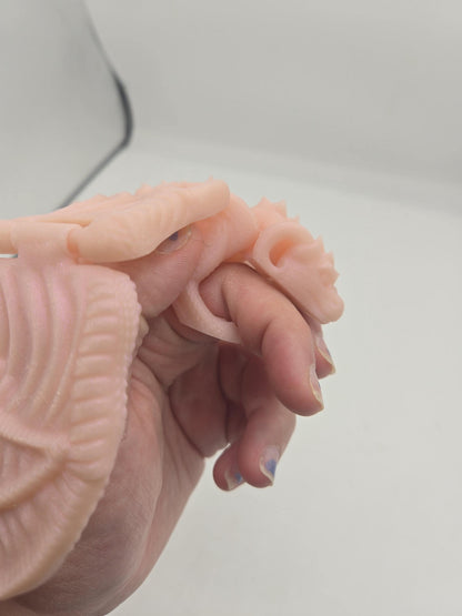 Close-up of baby dragon finger puppet hugging a finger with its head and front paws, puppet-style grip