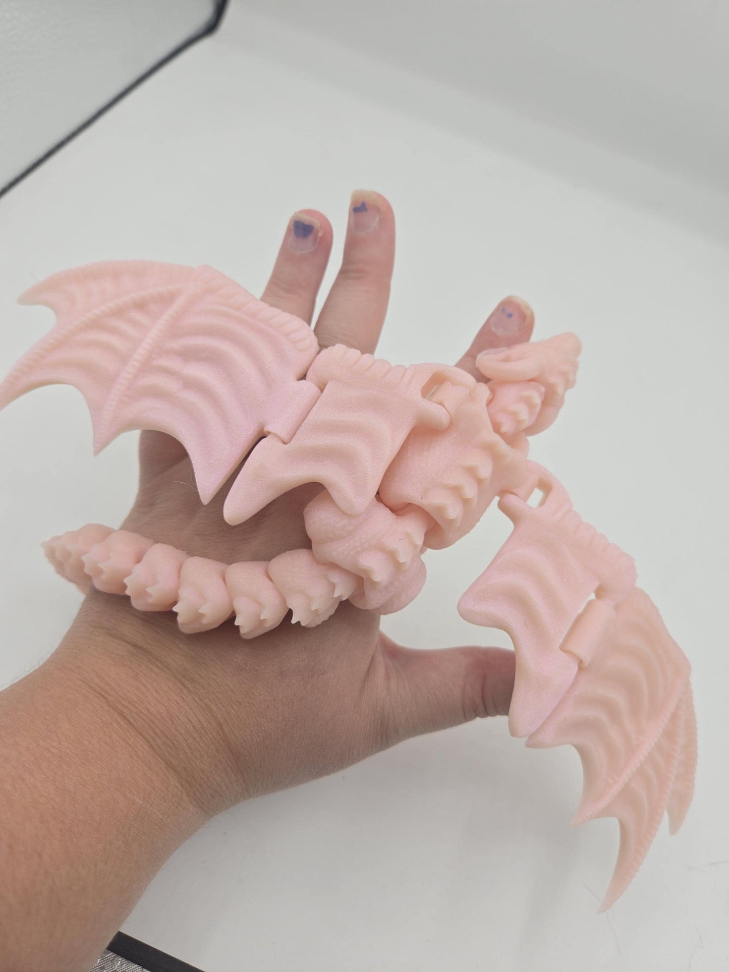 Pale pink baby dragon finger puppet resting in an open palm showing articulated tail and spread wings