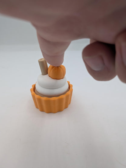Finger pressing the top of the pumpkin spice cupcake to demonstrate the hidden clicker fidget