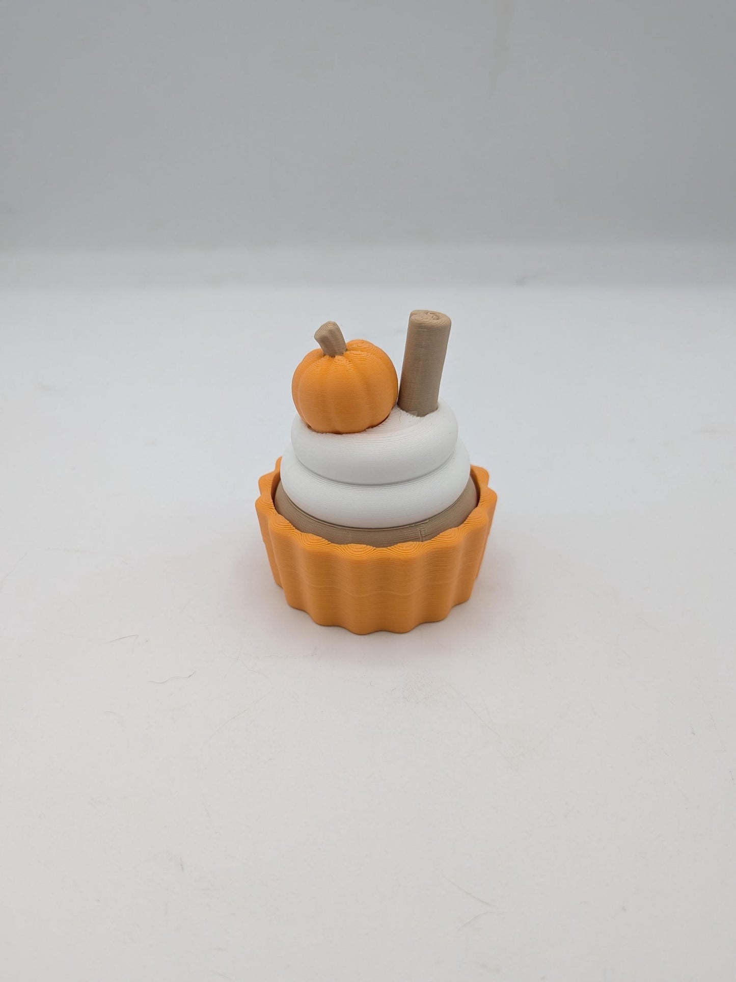 Angled view of pumpkin spice cupcake clicker with white frosting rings, mini pumpkin, and cinnamon stick