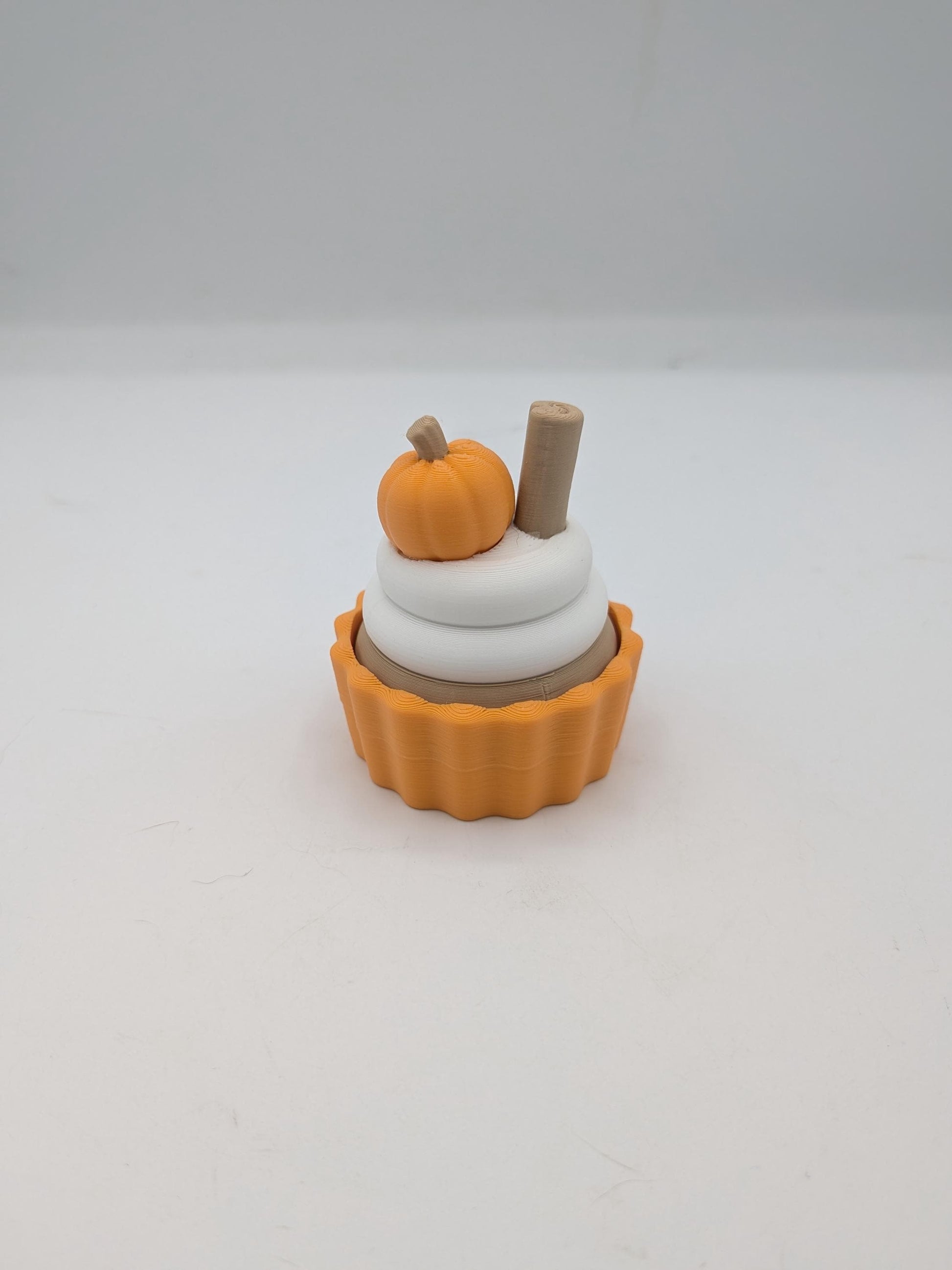 Angled view of pumpkin spice cupcake clicker with white frosting rings, mini pumpkin, and cinnamon stick