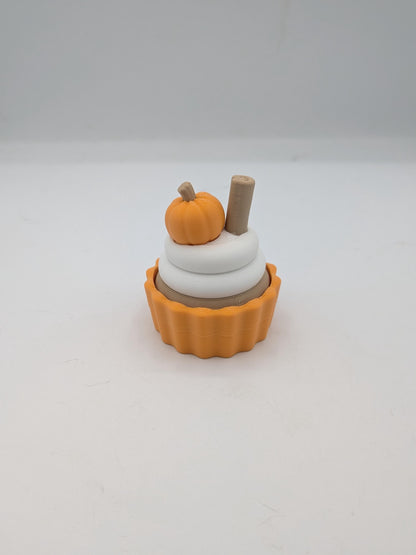 Angled view of pumpkin spice cupcake clicker with white frosting rings, mini pumpkin, and cinnamon stick