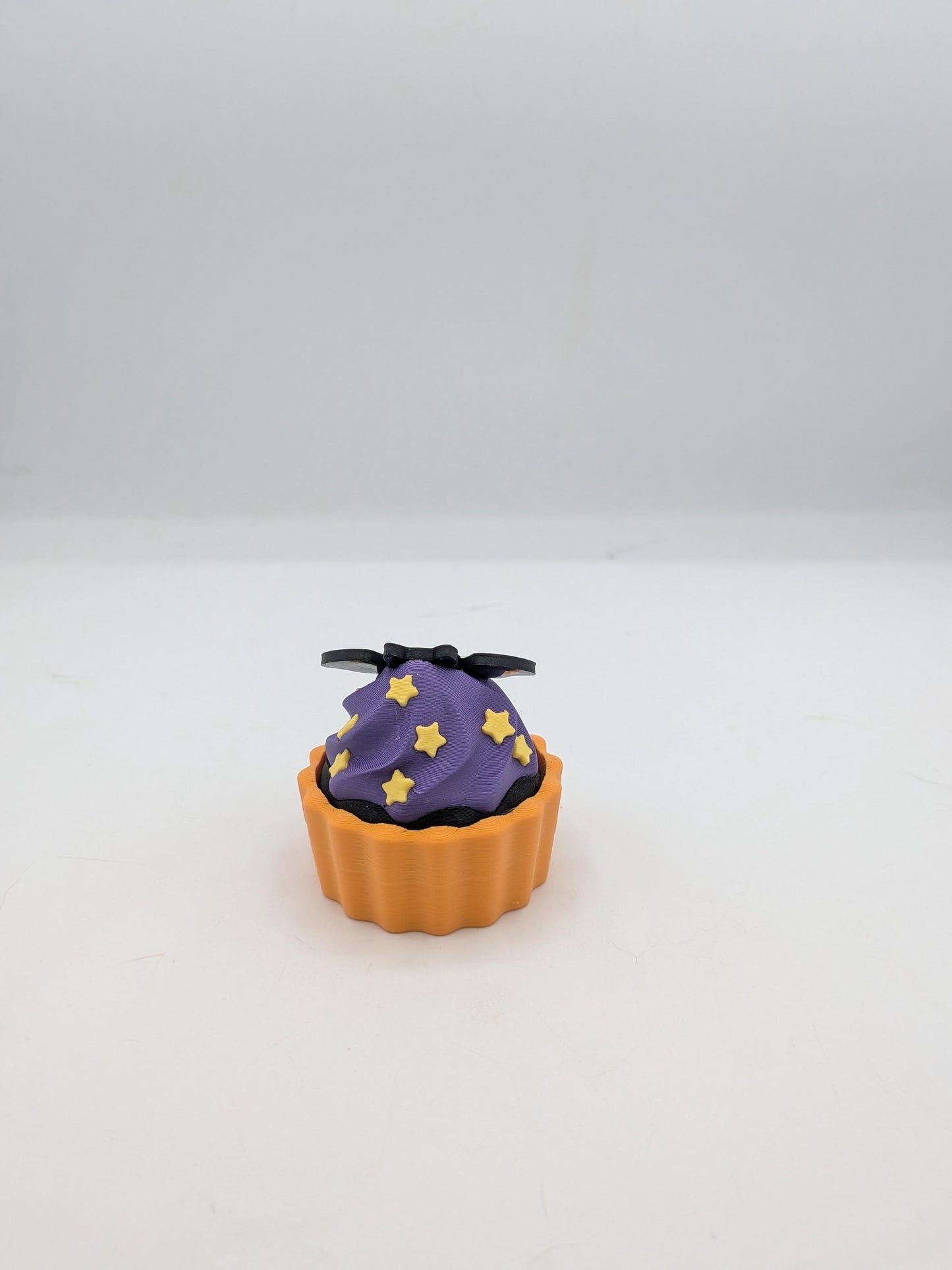 Angled view of bat cupcake clicker fidget showing yellow star sprinkles on purple frosting swirl