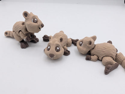Three mini quokka flexi 3D prints in tan and brown — one sitting upright, two lying flat showing articulated segments