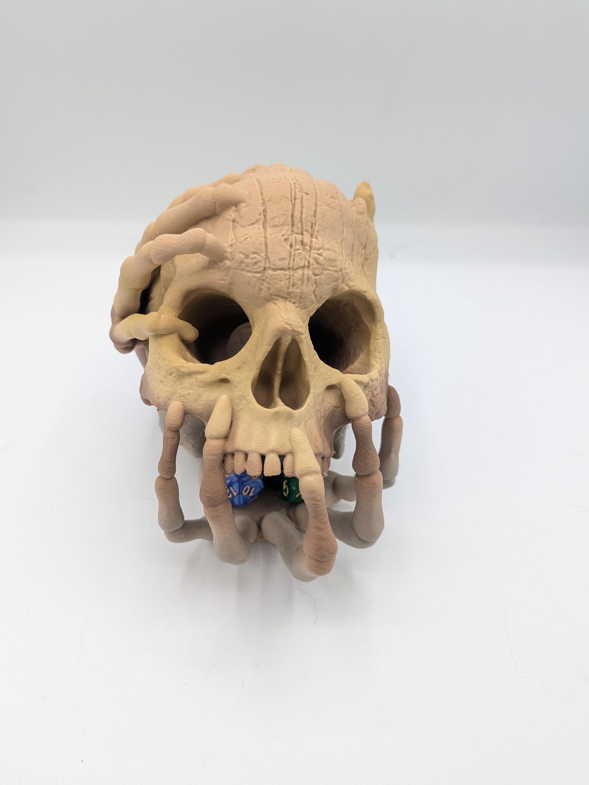 Skull skeletal hand dice tower 3D printed in Ziro Wood gradient — front view with polyhedral dice in the bone hand tray by the mouth