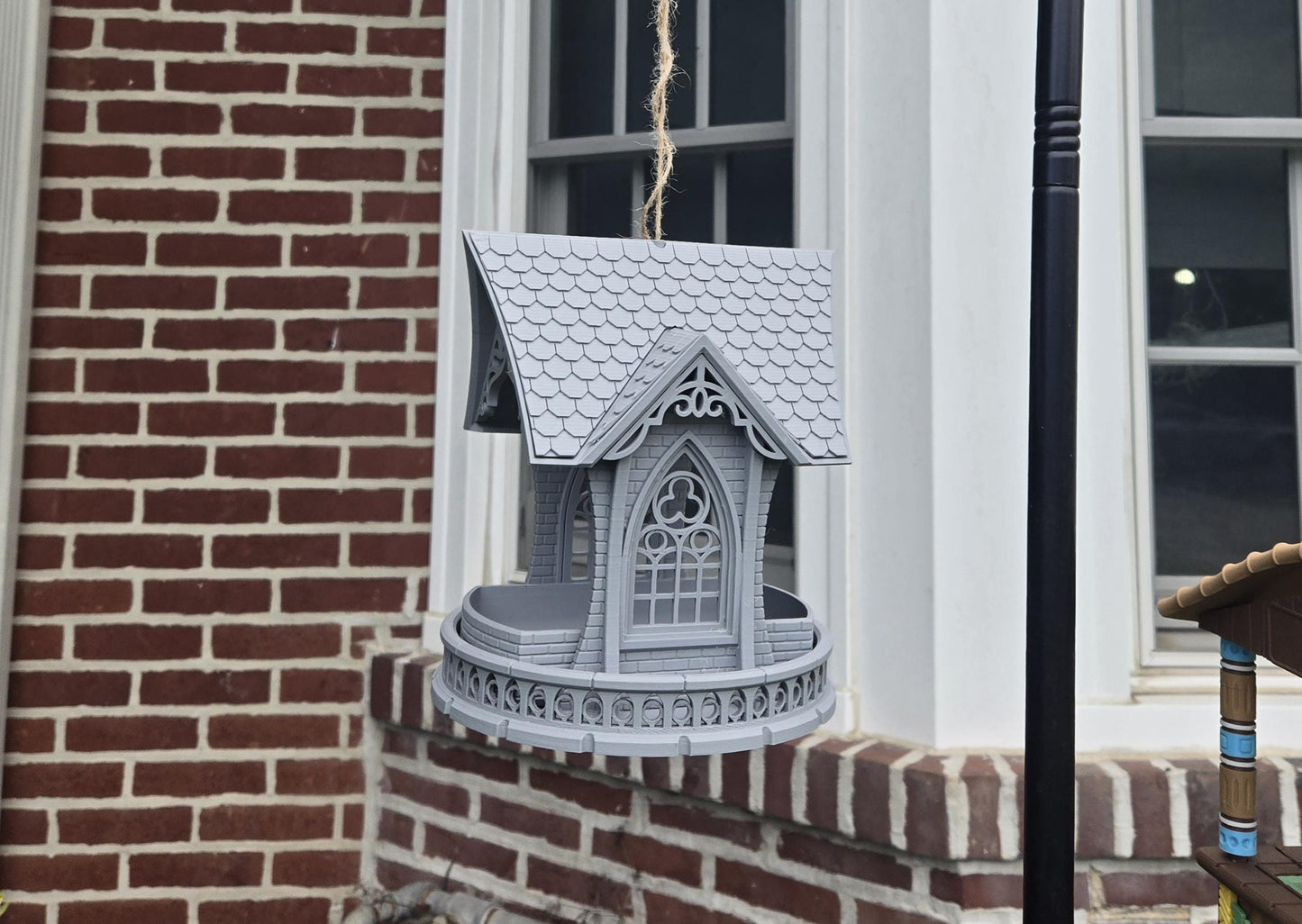 Gothic church bird feeder hanging outdoors against a brick wall — shingled roof and cathedral window