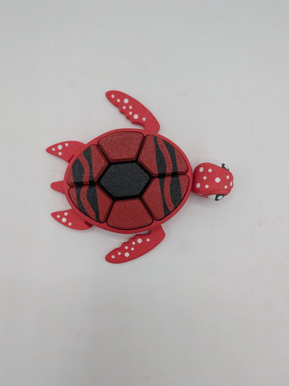 Top view of red turtle clicker fidget with black striped shell showing the seven clicker key segments
