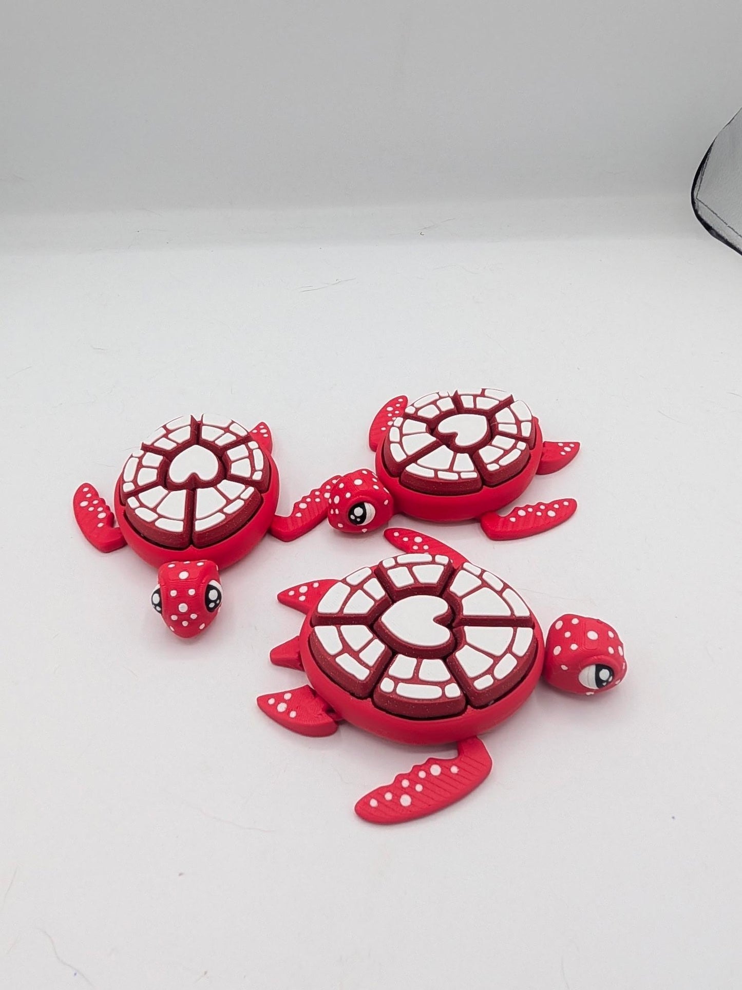 Three red and white turtle mechanical clicker fidgets with heart design shells and spotted flippers, 3D printed