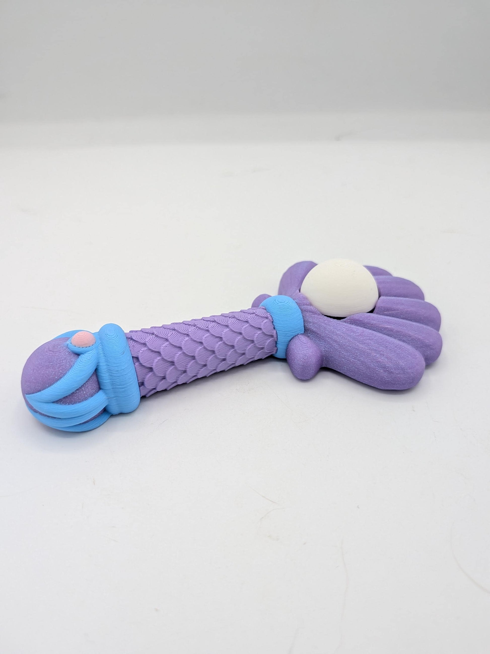 Side view of mermaid wand clicker fidget showing ribbed shell back, scaled handle, and blue wave details