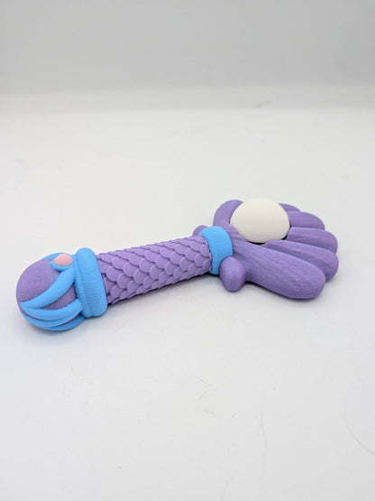 Side view of mermaid wand clicker fidget showing ribbed shell back, scaled handle, and blue wave details