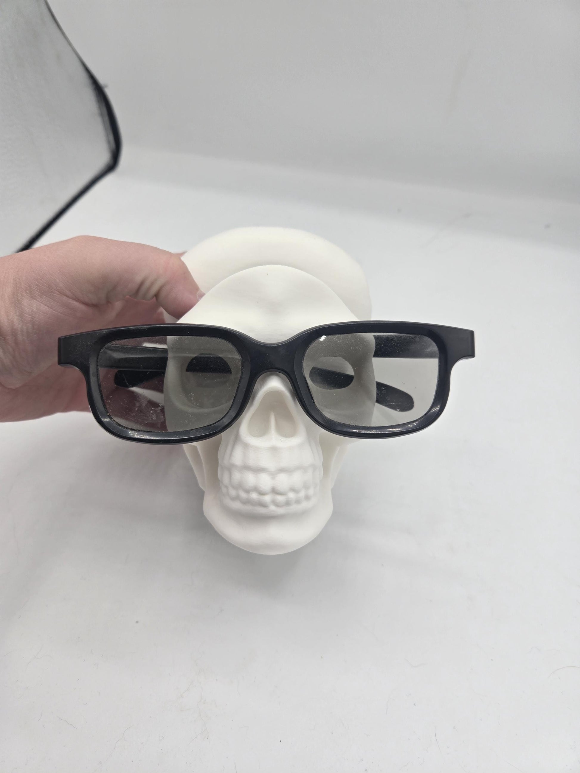 Hand placing black eyeglasses onto the white human skull holder, front view