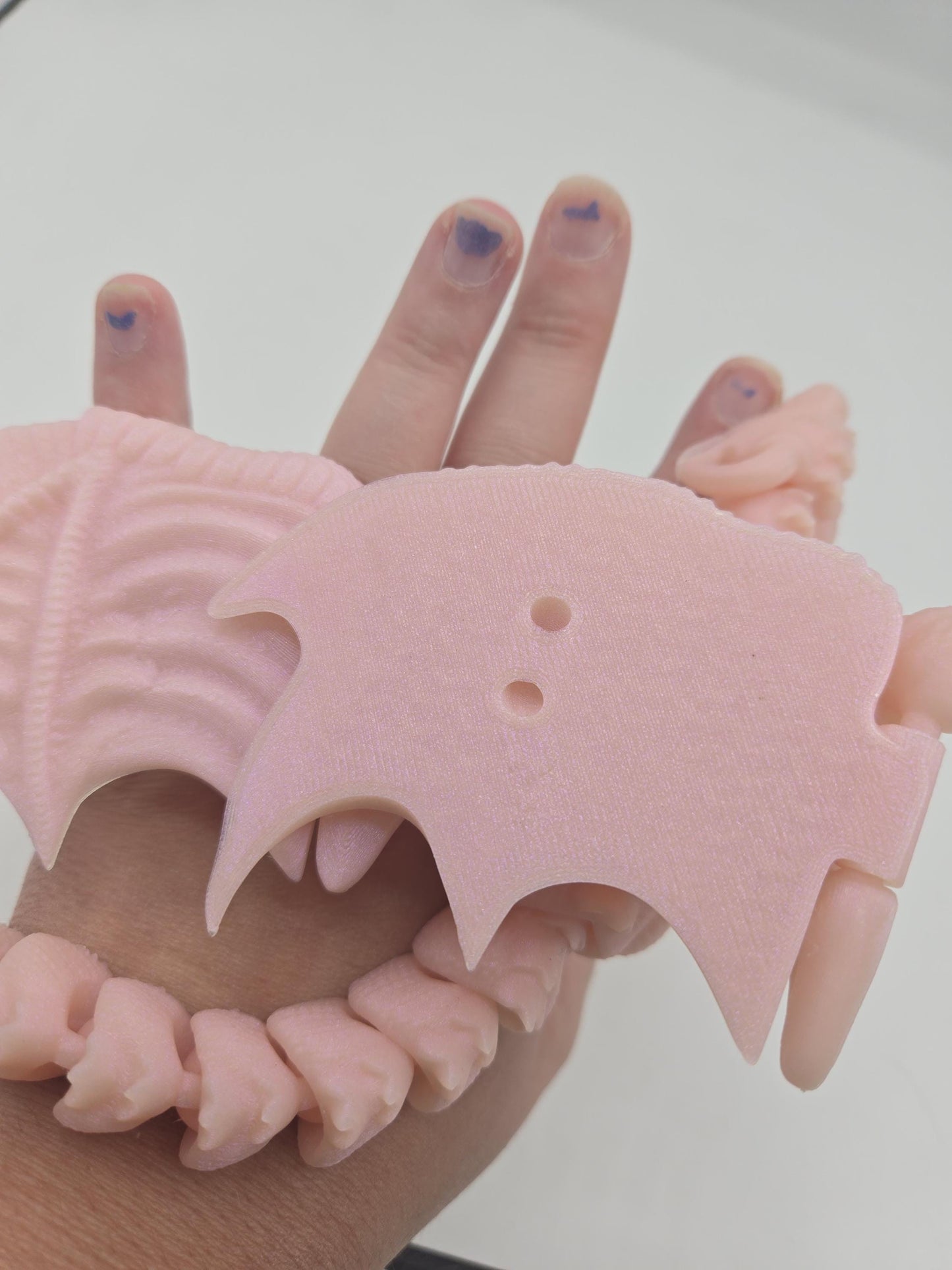 Close-up of baby dragon finger puppet wing showing small holes for adding elastic, pale pink 3D print