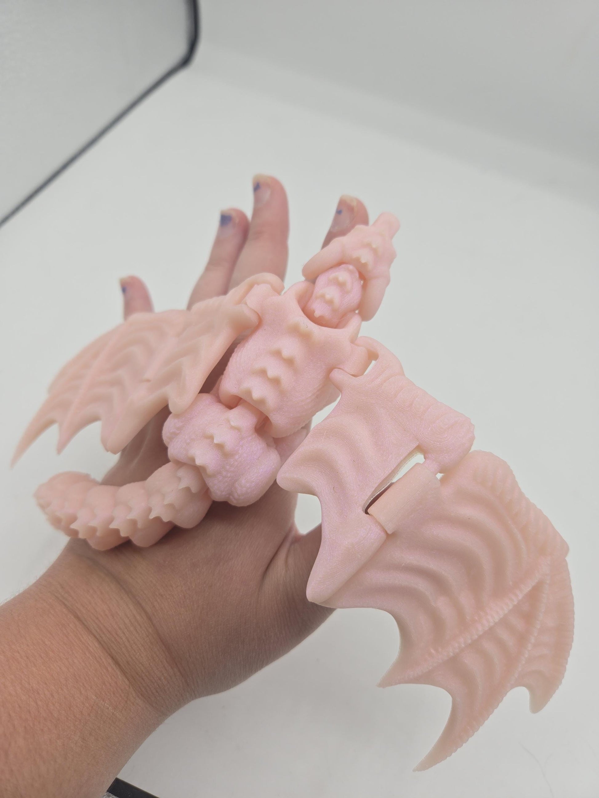 Baby dragon finger puppet flexi figurine in pale pink held in hand with textured wings spread, 3D printed