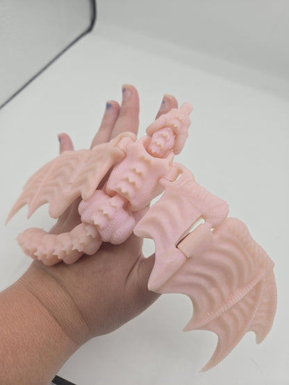 Baby dragon finger puppet flexi figurine in pale pink held in hand with textured wings spread, 3D printed