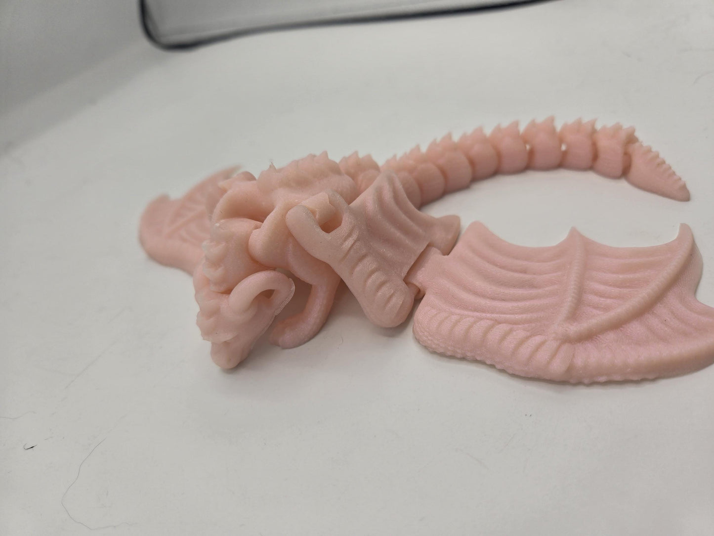 Baby dragon finger puppet lying on a desk, side view of articulated segmented tail and wing detail