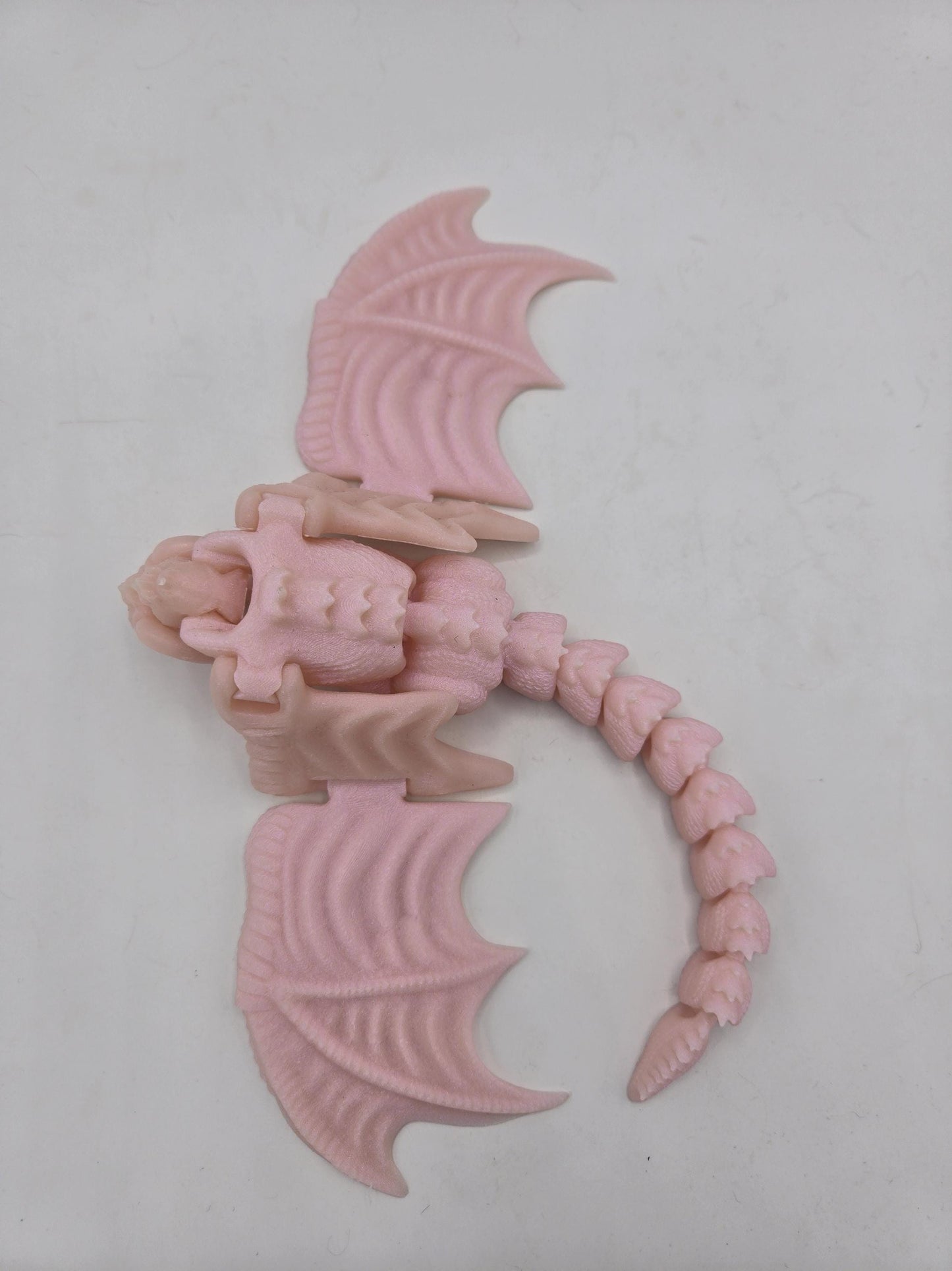 Top view of pale pink baby dragon finger puppet with wings spread and curved articulated tail