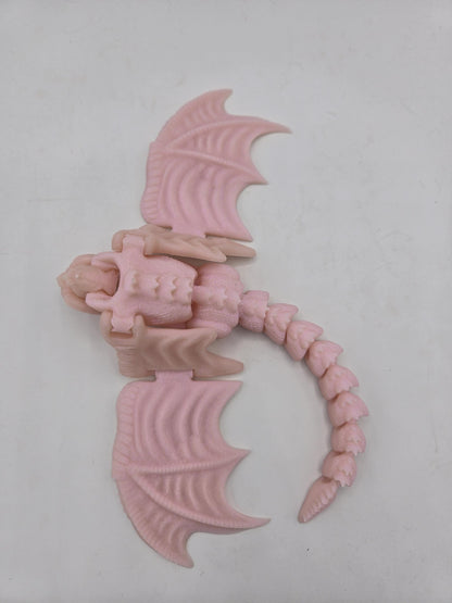 Top view of pale pink baby dragon finger puppet with wings spread and curved articulated tail
