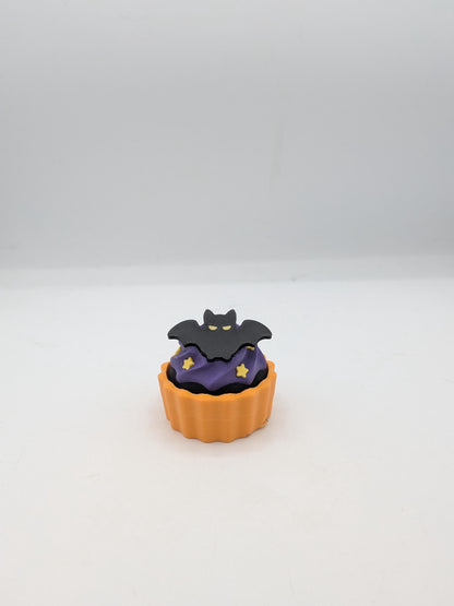 Bat Halloween cupcake clicker fidget with black bat topper on purple frosting in an orange tin