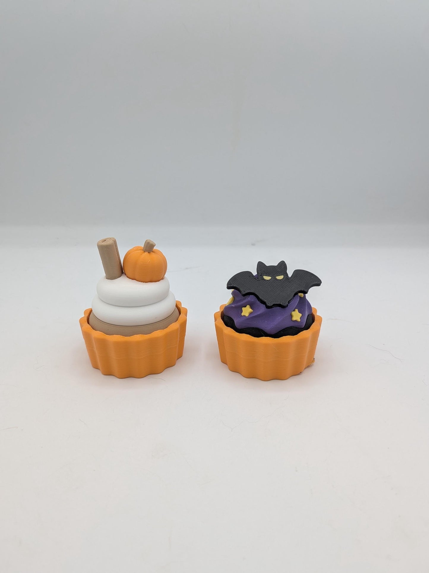 Pumpkin spice and bat Halloween cupcake clicker fidgets side by side in orange tins