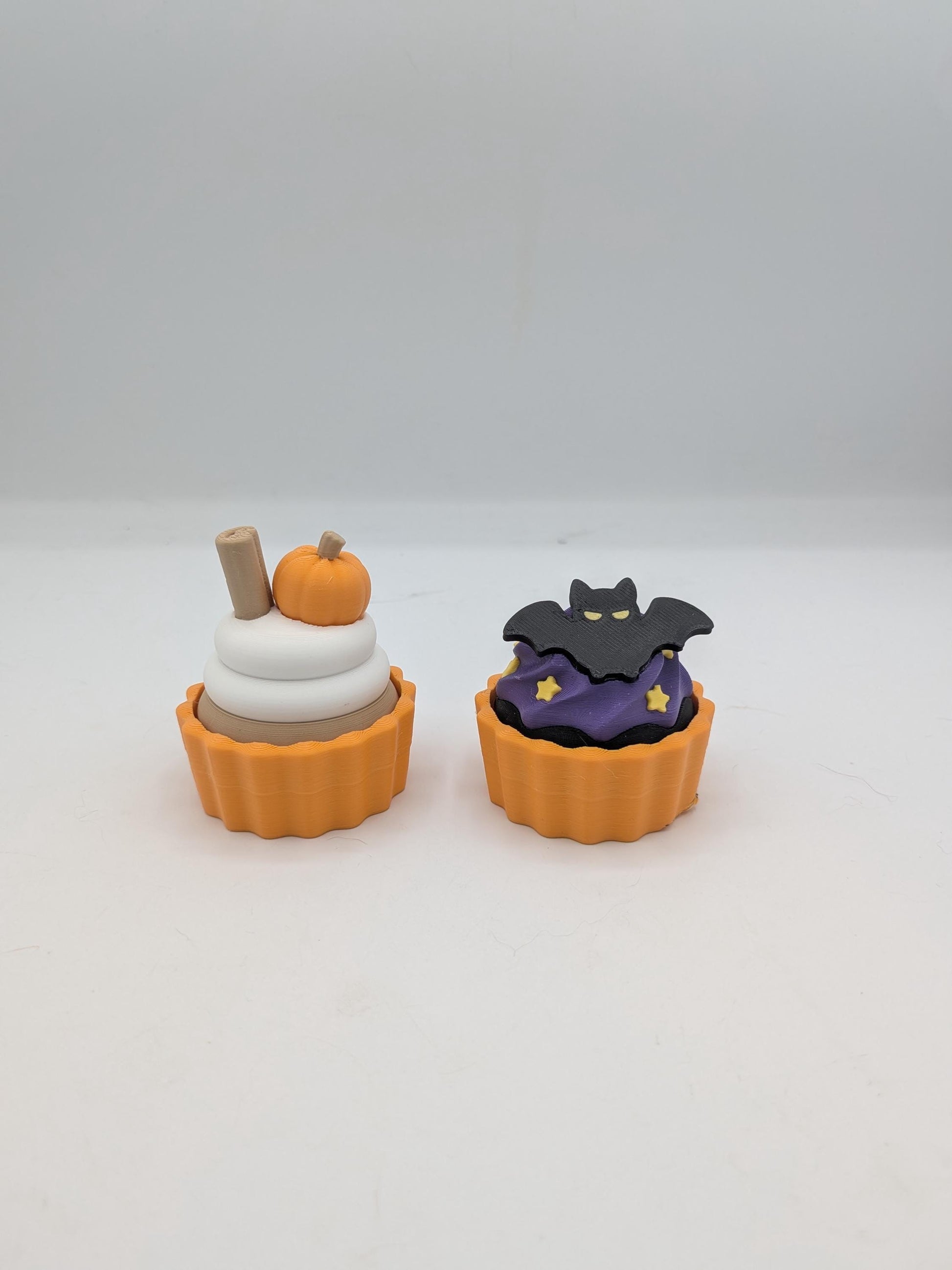 Pumpkin spice and bat Halloween cupcake clicker fidgets side by side in orange tins