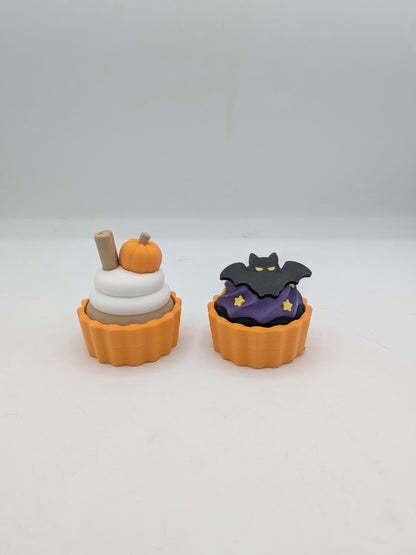 Pumpkin spice and bat Halloween cupcake clicker fidgets side by side in orange tins