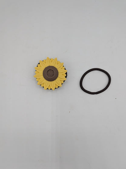 Sunflower hair tie holder top view — yellow petals around a textured brown center, with a brown hair tie beside it for scale