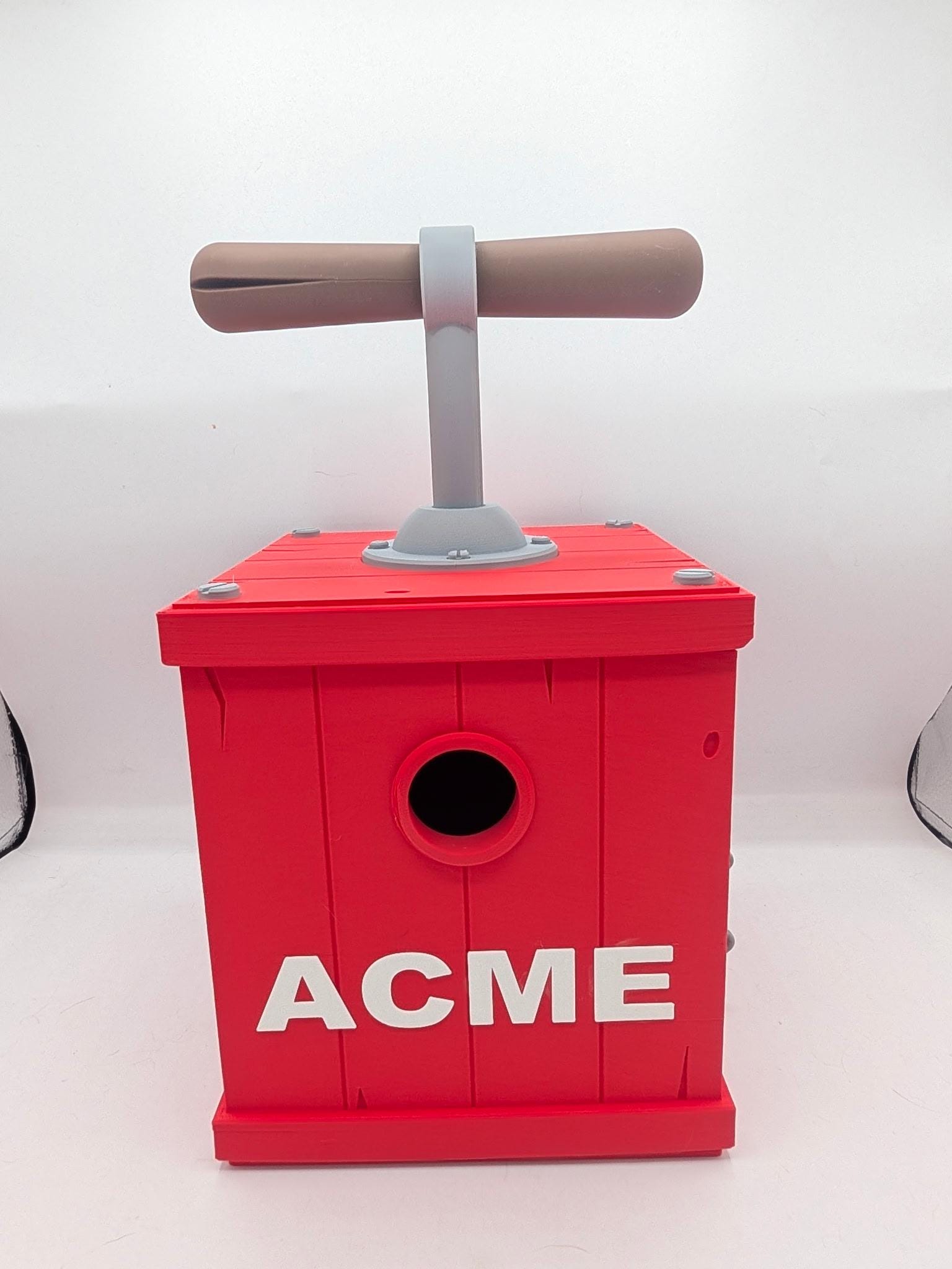 Red cartoon TNT detonator birdhouse 3D print, front view with round entrance hole, gray plunger handle, and ACME lettering