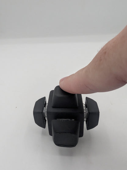 Finger pressing the top keycap of the black clicker cube key switch fidget, 3D printed