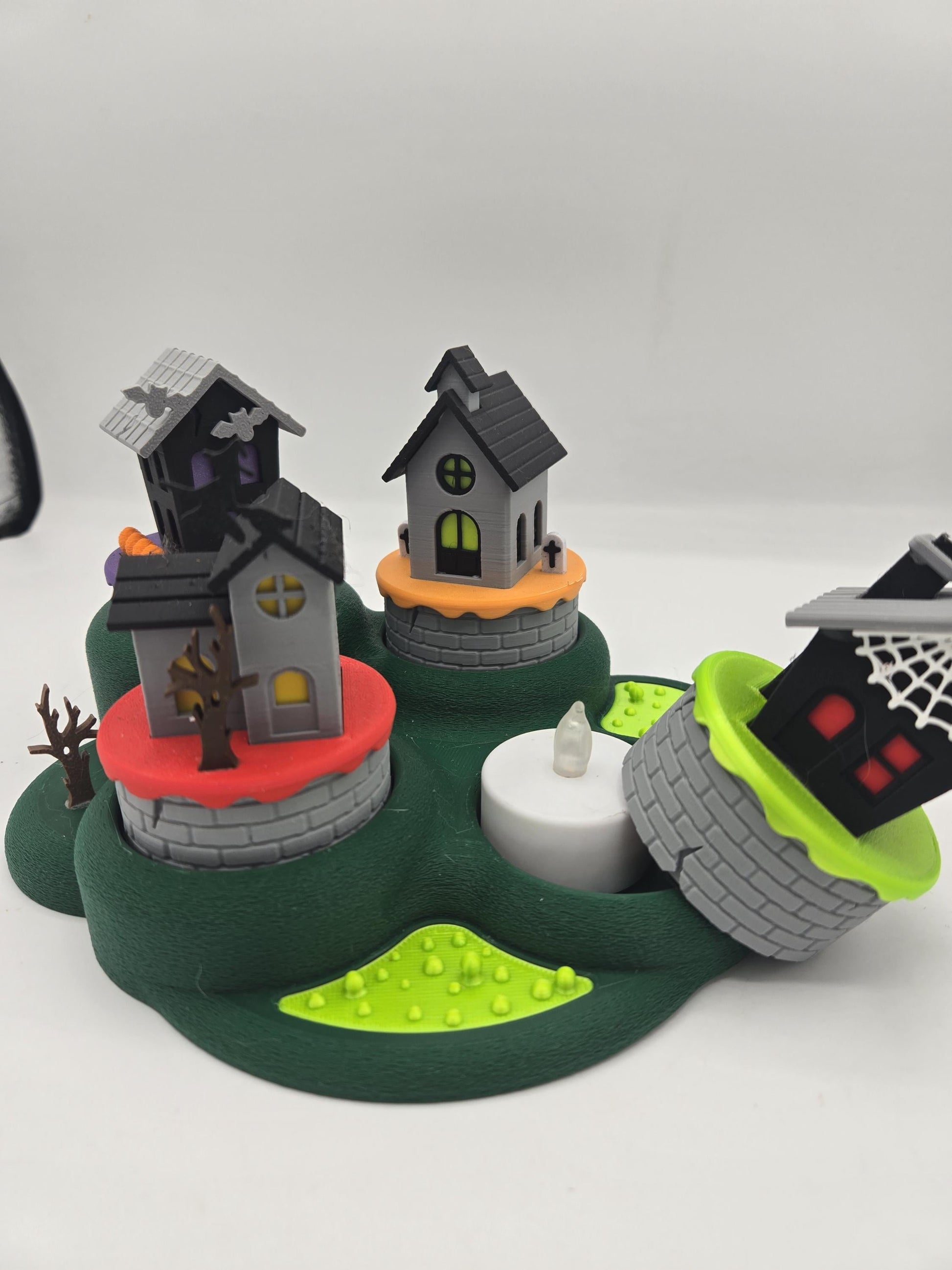 Halloween tealight village with one house tipped off its base, showing the LED tealight slot beneath the 3D printed buildings