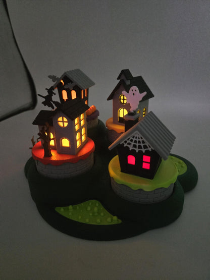 Halloween mini village glowing at night — LED tealights lighting the windows of all four 3D printed haunted houses