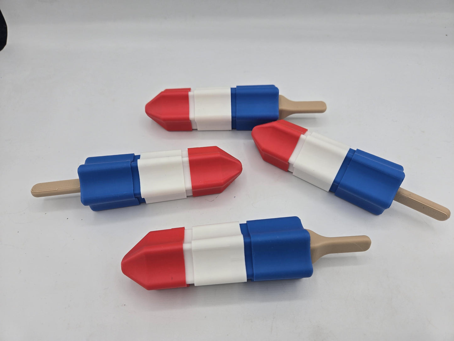 Four 3D printed rocket popsicle clickers with tan popsicle sticks arranged on a white background
