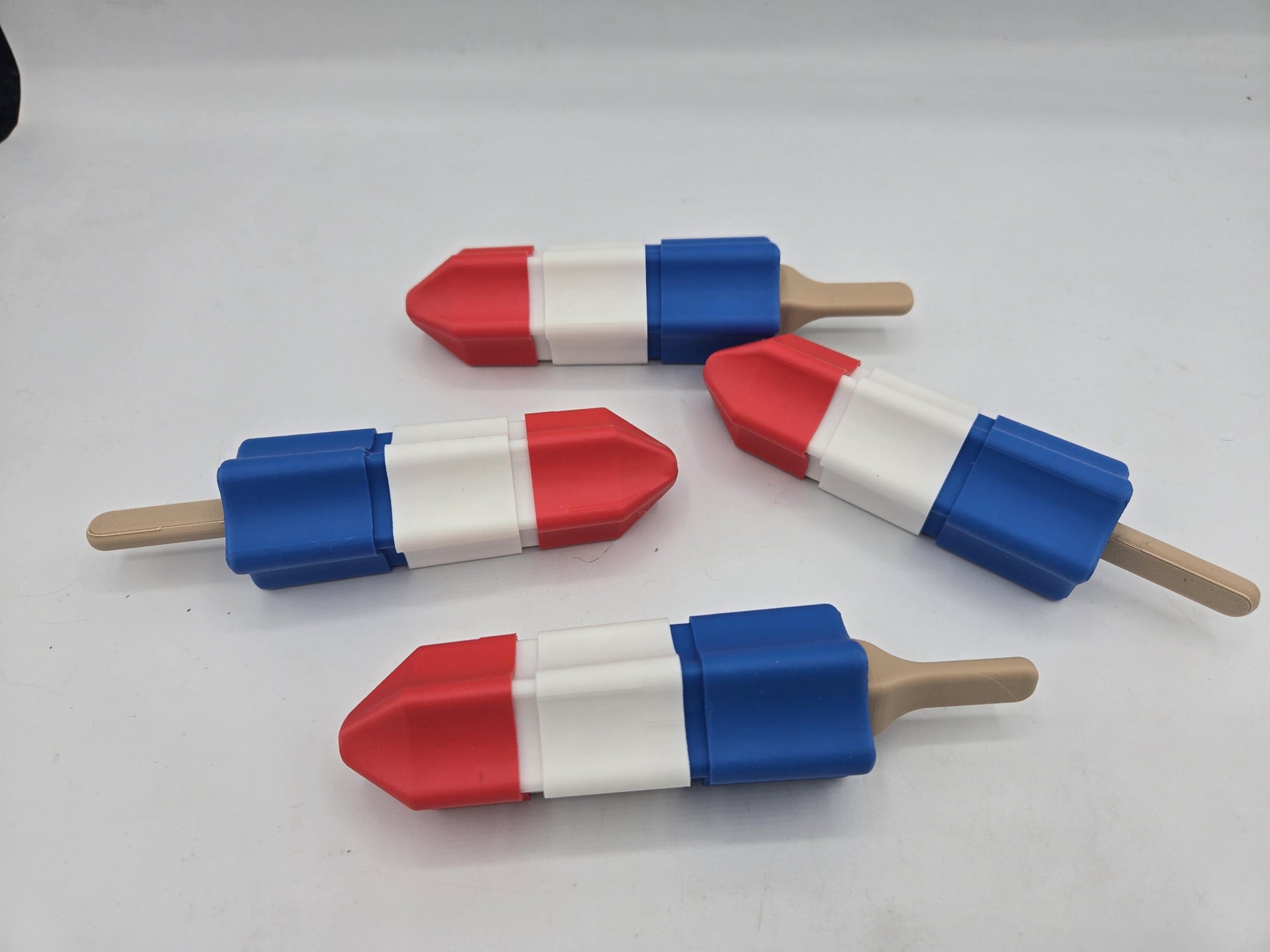 Four 3D printed rocket popsicle clickers with tan popsicle sticks arranged on a white background