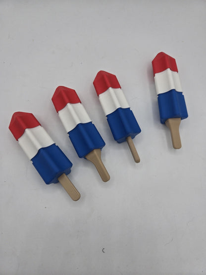 Four summer popsicle clickers laid out in a diagonal row, each showing the red tip, white middle, and blue base with stick