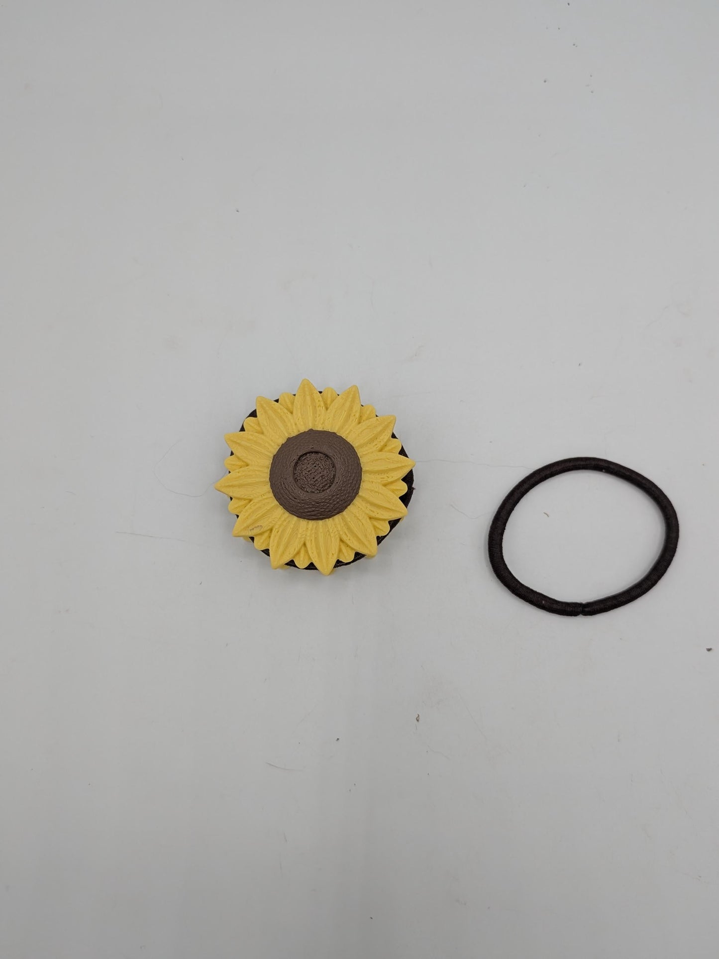 Top-down view of the sunflower hair tie holder next to a brown elastic hair tie, showing the flower cap that keeps stored ties in place
