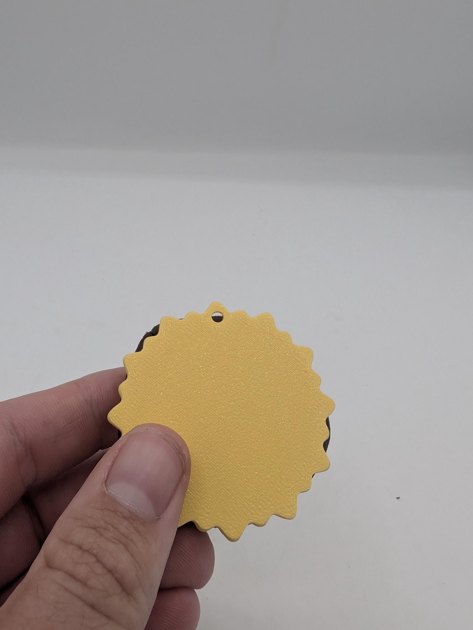 Back of the sunflower hair tie holder held in a hand, showing the scalloped yellow base with a small hanging hole for a keychain or clip