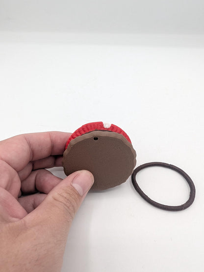 Back of the mushroom hair tie holder held in a hand, showing the smooth brown base with a small hanging hole