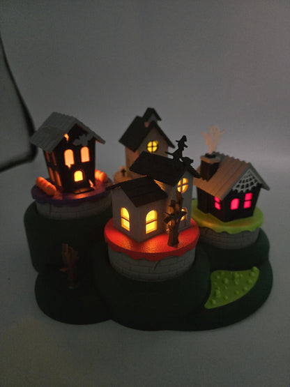 All four Halloween village houses lit at night with glowing orange, yellow, and pink windows from LED tealights