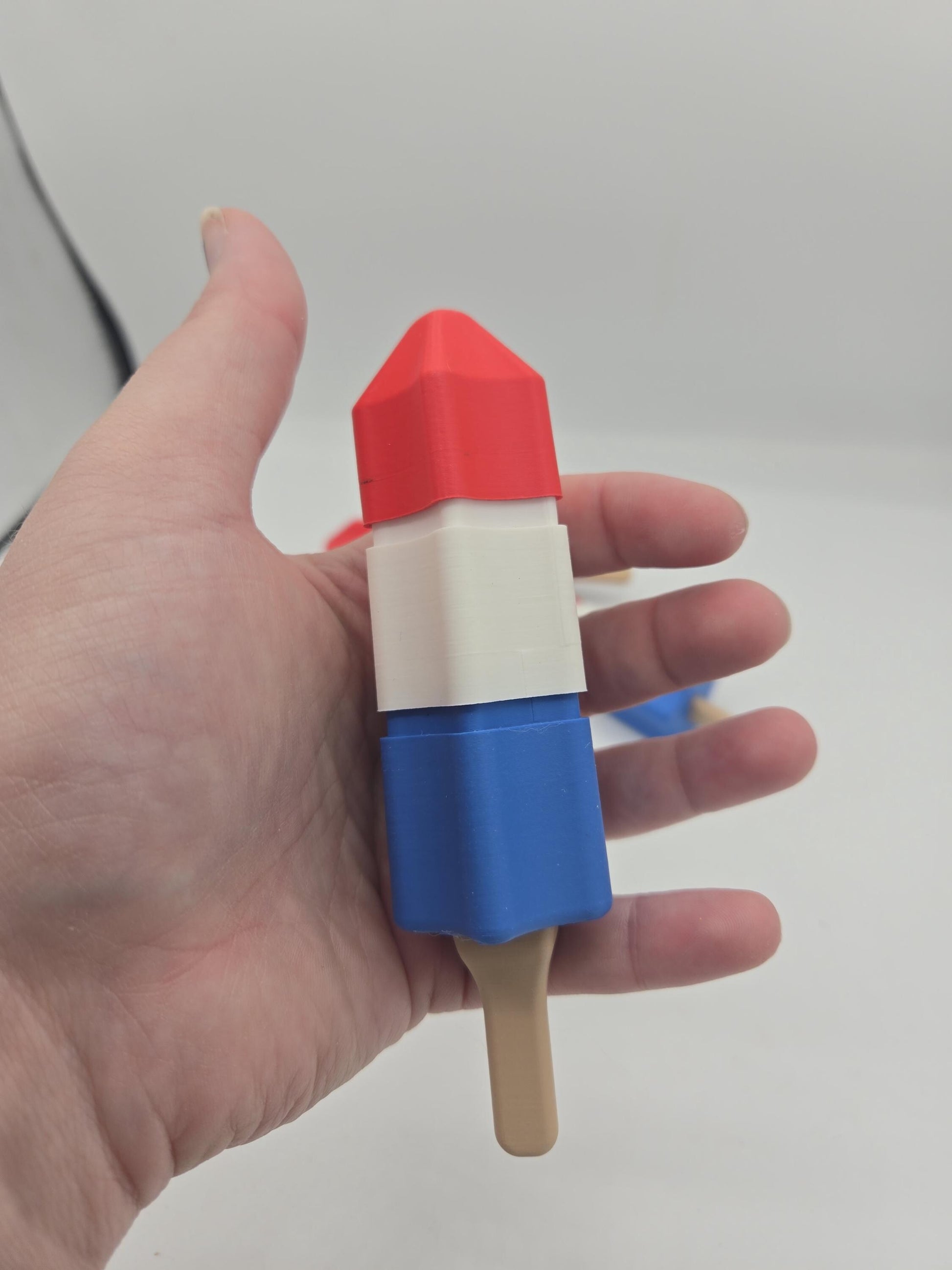 Summer popsicle mechanical key fidget clicker held in a hand for size — palm-sized red, white, and blue 3D printed toy