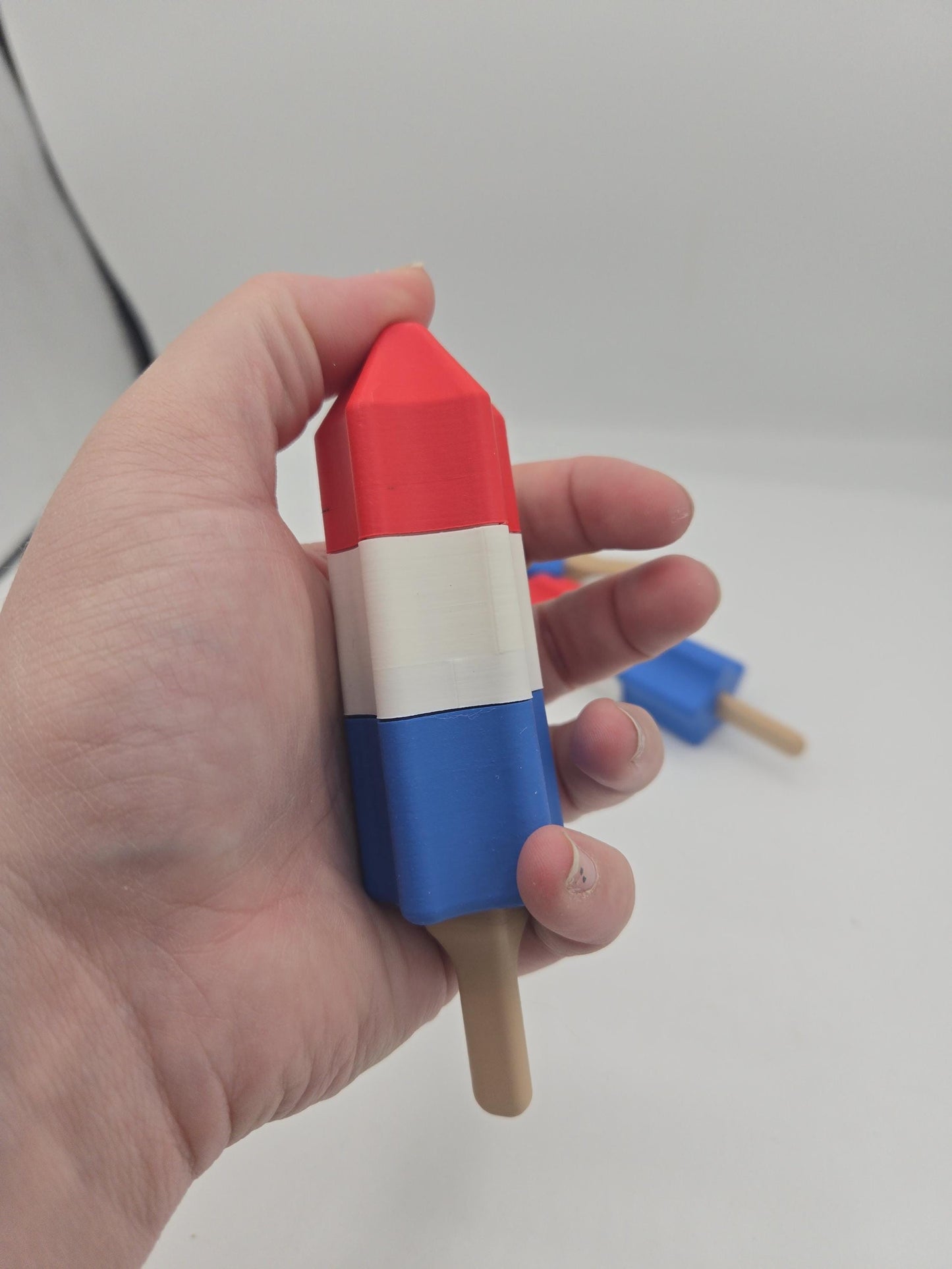 Rocket popsicle clicker held in a hand showing the red tip, with more clickers on the table behind