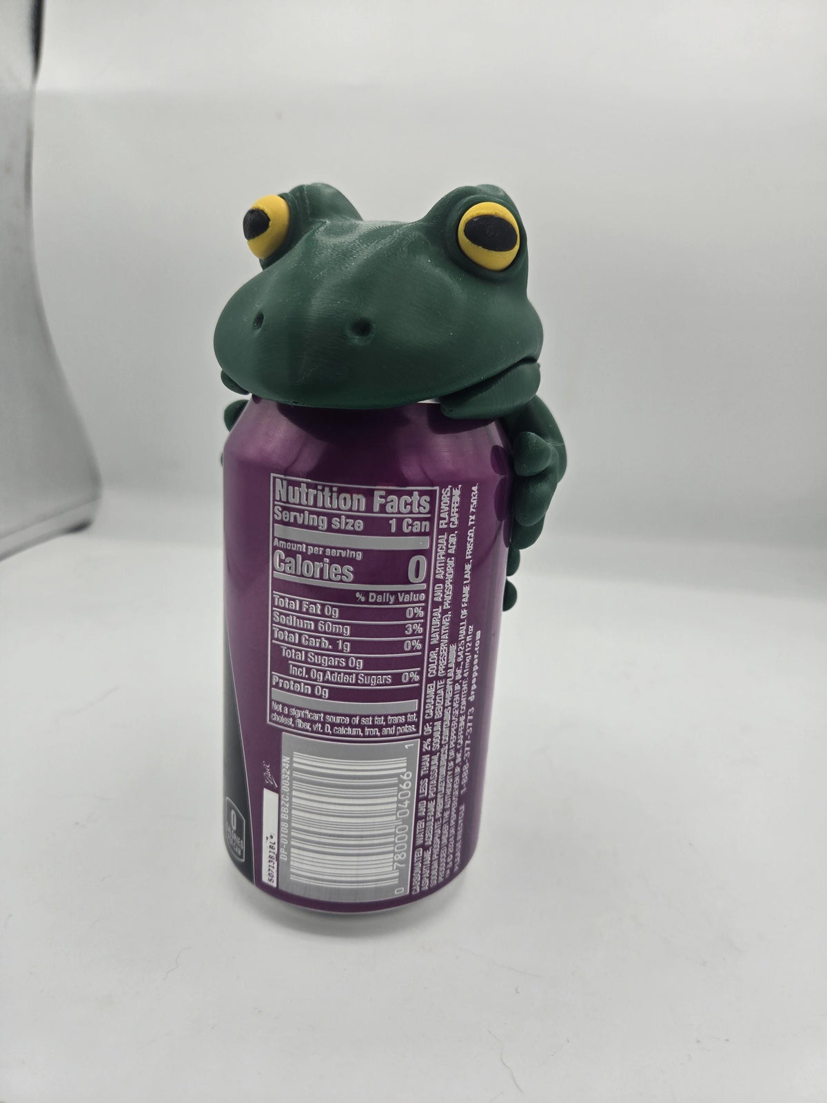 Frog Can Cover 3D print front view — green frog face with big yellow eyes resting over the top of a 12oz can, arms wrapped around the sides