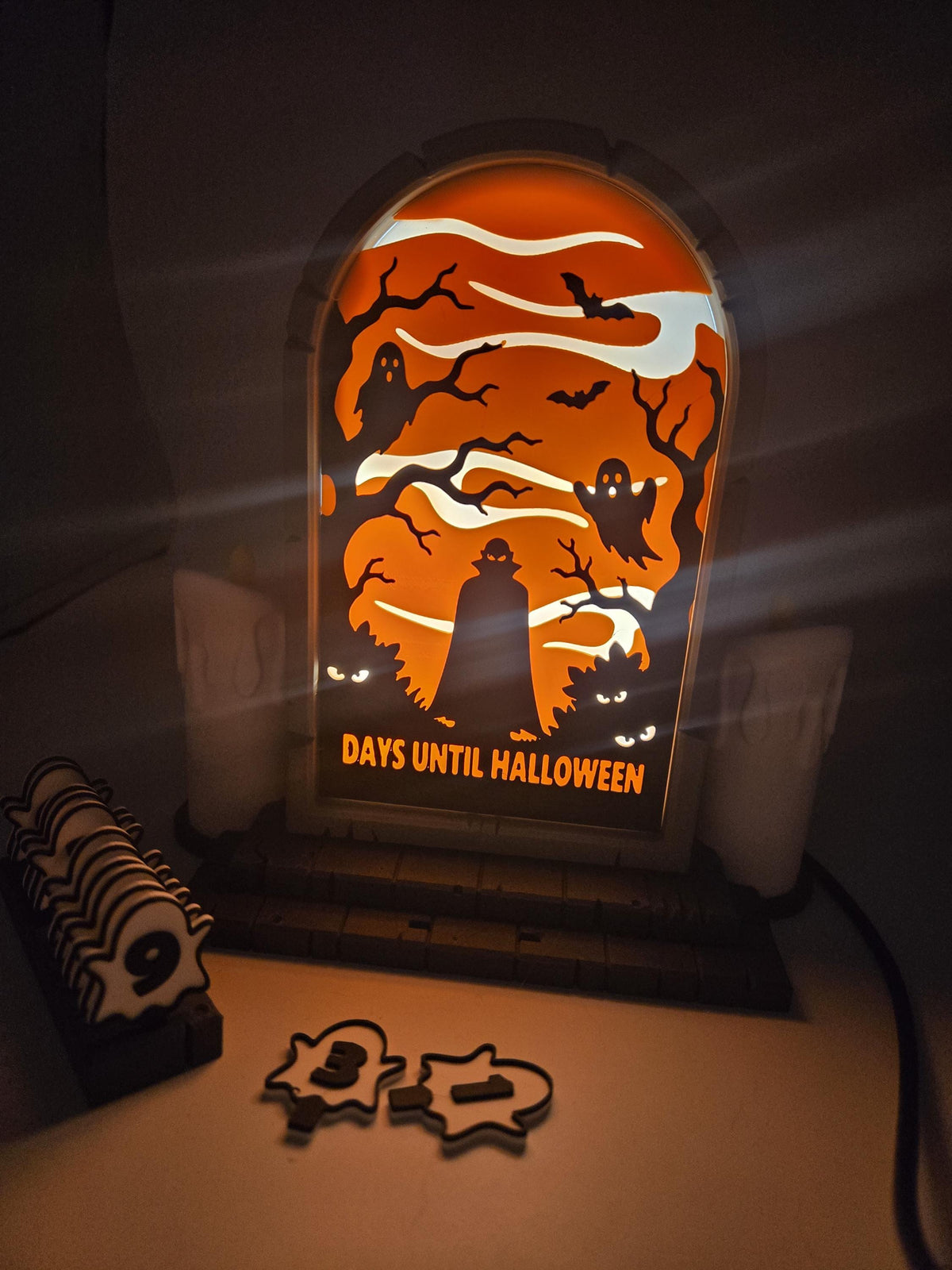Vampire Halloween Countdown pre-lit version glowing in a dark room — orange backlit vampire scene with the ghost number tiles and spare tile rack in front