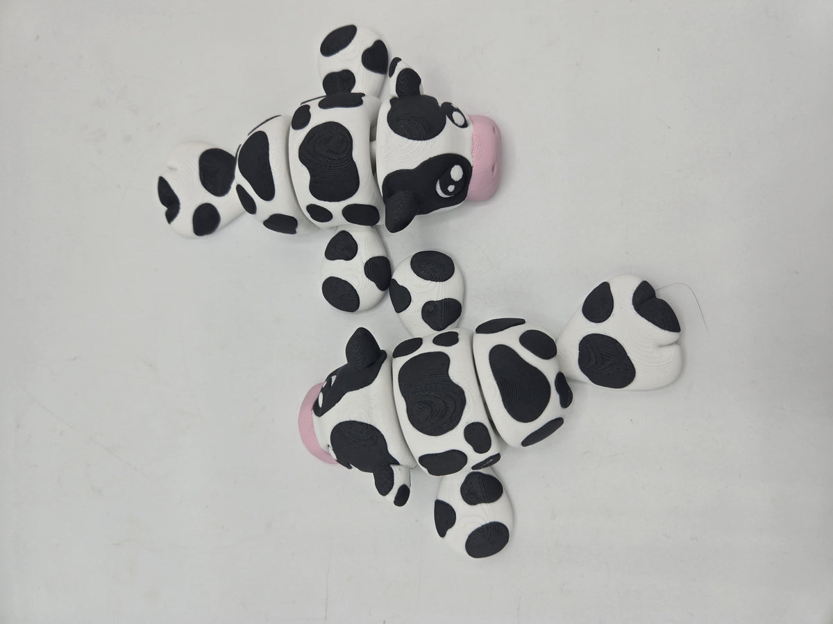Two Sea Cow Manatee flexi 3D prints flat lay from above, showing black and white cow spots, pink noses, and articulated joints