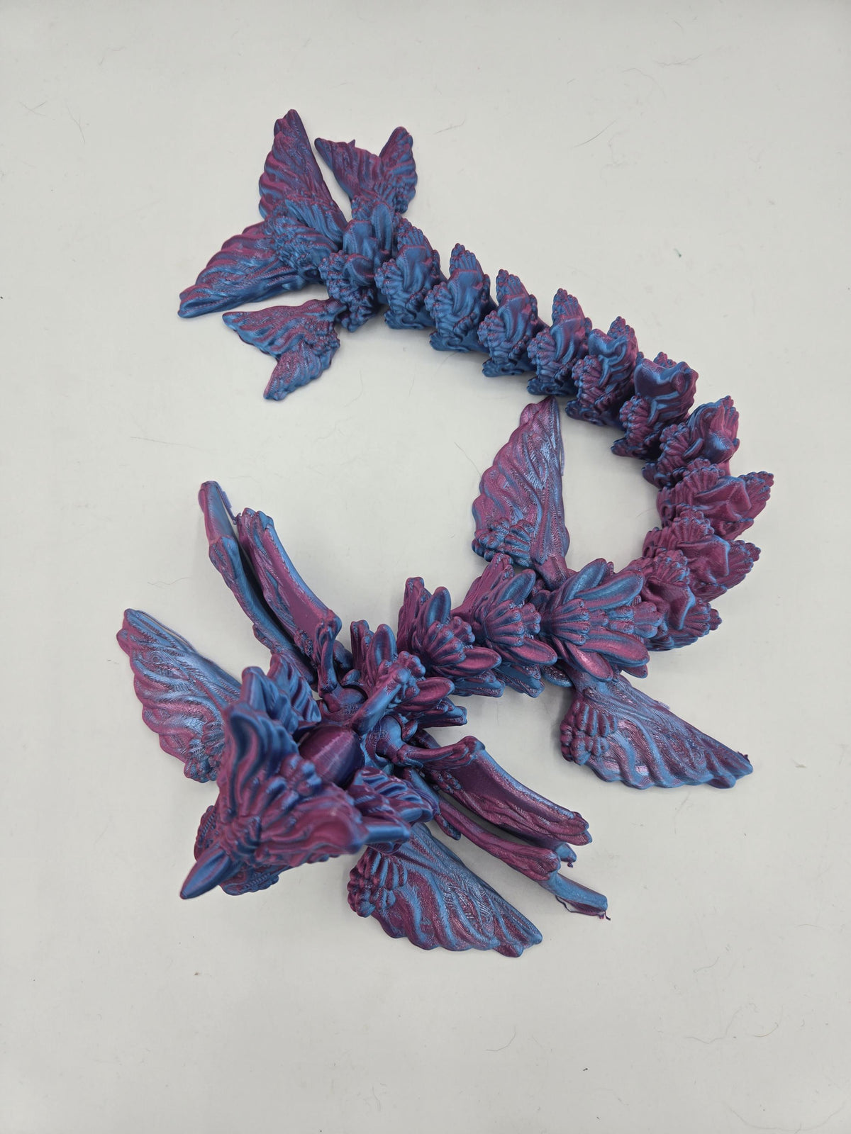 Ocean Sea Dragon flexi 3D print top-down view showing the full articulated body coiled in an S curve with tail fins and finned wings, Blue-Purple Dual