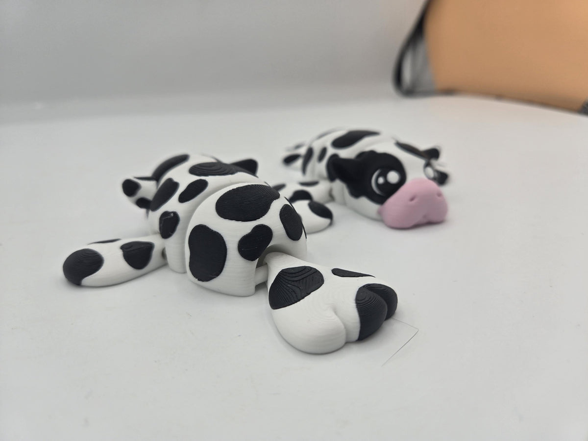 Two Sea Cow Manatee flexi 3D prints in cow-spot colors, one seen from behind showing the articulated tail and body segments
